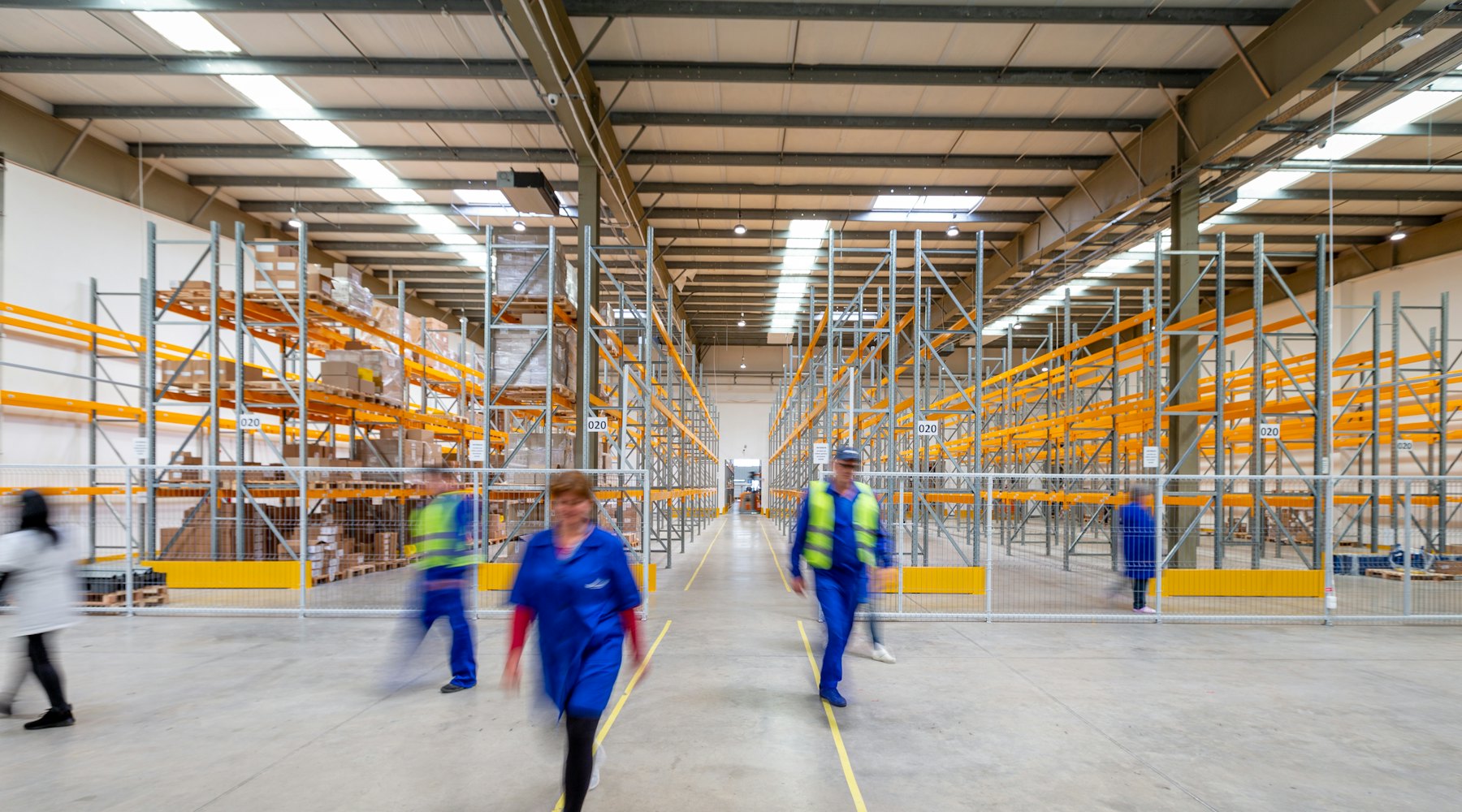 Warehouse aisle lined with pallet racking as staff move stock